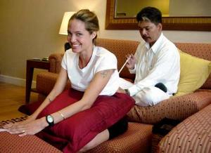 U.S. actress Angelina Jolie smiles while getting a tattoo of a tiger from Thai artist Sompong Kanphai during her visit to Bangkok on July 8, 2004. Jolie was in Thailand after her visit to Cambodia. Picture taken July 8, 2004. THAILAND OUT NO SALES NO ARCHIVES REUTERS/Nation