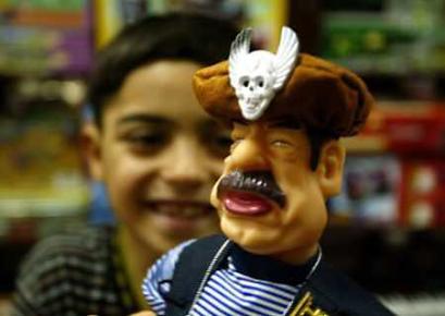 An Iraqi boy smiles while looking at a display of Saddam Hussein (news - web sites) dolls in a Baghdad toyshop June 29, 2004. Iraqis used to dance to his tune, but in Baghdad toy shops a chubby, gun-toting Saddam Hussein doll now wiggles his hips to the 'Hippy Hippy Shake.' Toy stores around Baghdad are doing a quick trade in dancing Saddam dolls -- foot-high battery-powered puppets of the former president, kitted out in full insurgent regalia, who swing their hips to cheesy pop music at the flick of a switch. (Zohra Bensemra/Reuters)